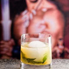 a close up of a drink in a glass on a table with a poster behind it