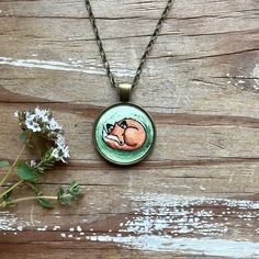 a necklace with an image of a sleeping cat on it and flowers in the foreground