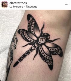 a black and white dragonfly tattoo on the left leg, with an intricate design