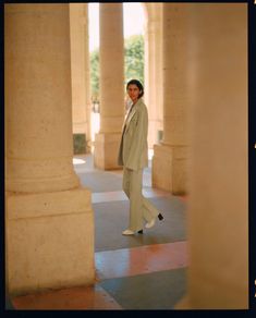 a woman in a white suit is standing under some pillars