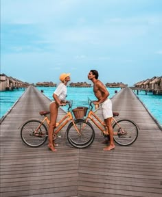 two people standing on a pier next to bikes with the ocean in the back ground