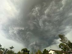 a very large cloud is in the sky over some houses and trees on a cloudy day