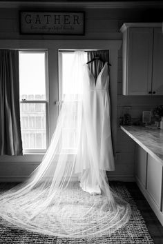 a wedding dress hanging in front of a window with the bride's veil pulled back