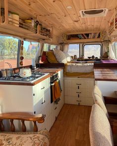 the interior of a camper with wood flooring and white cabinets, including a stove top oven