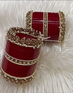 two red and gold bracelets sitting on top of a white fur covered floor next to each other