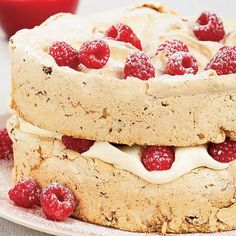 a cake with raspberries and cream frosting on top is sitting on a plate