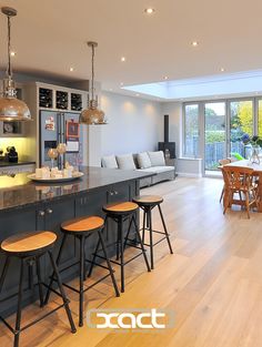 an open kitchen and living room with wood flooring in the middle, along with large sliding glass doors leading outside