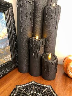 three candles sitting on top of a wooden table next to a painting and framed photograph