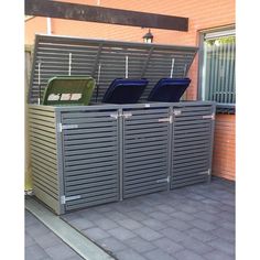 two metal trash cans sitting on top of a brick floor next to a wall with shutters