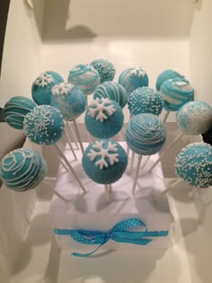 blue and white cake pops with snowflakes on them sitting in a box, ready to be eaten