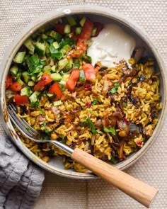 a bowl filled with rice and vegetables next to a wooden utensil on top of a table