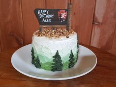 a birthday cake on a plate with a happy birthday sign in the middle and pine trees around it