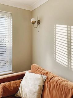 a brown couch sitting next to a window with blinds on it's windowsill