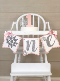 a baby's first birthday cake sitting on top of a wooden chair with snowflakes