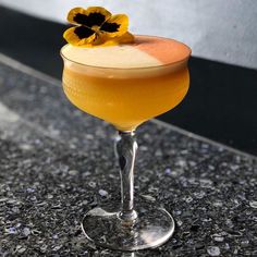 an orange cocktail with a yellow flower on the top sits on a countertop in front of a black and white wall