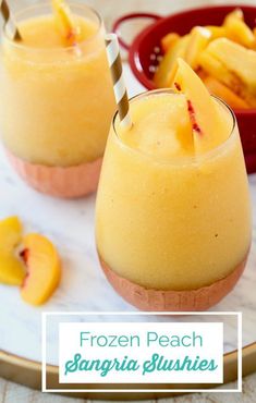 two glasses filled with yellow liquid on top of a white marble plate next to sliced peaches