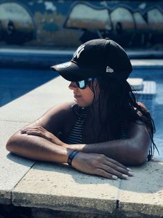 a woman sitting on the edge of a swimming pool wearing a hat and sun glasses