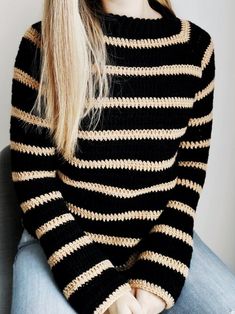 a woman with long blonde hair wearing a black and gold striped sweater sitting in a chair