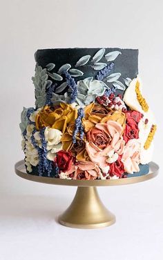 a multi - colored cake with flowers on top is sitting on a gold plate against a white background