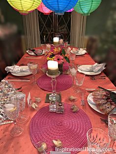 the table is set with plates, silverware and colorful paper lantern lights above it