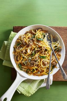 a white bowl filled with pasta and meat on top of a wooden cutting board next to a green napkin