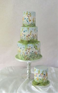 three tiered cake decorated with flowers and grass on a tablecloth covered table cloth