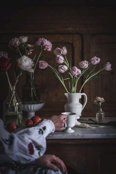 a woman sitting at a table with flowers in vases