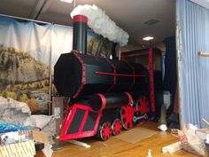 a black and red train sitting on top of a wooden floor next to a window