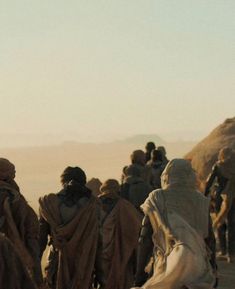 a group of people walking down a dirt road next to a hill covered in sand