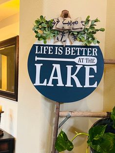 a sign that says life is better at the lake on a ladder next to a potted plant