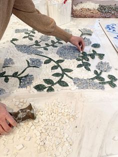 a person is working on some art work with glass and stone mosaics in the background