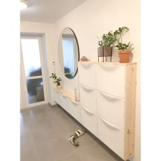 a white dresser with plants on top and a mirror in the corner next to it