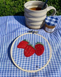 two strawberries on blue gingham tablecloth next to a cup of tea