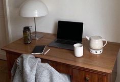 a laptop computer sitting on top of a wooden desk next to a lamp and cup