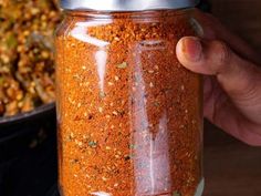 a person is holding a jar full of chili seasoning next to a bowl of other spices