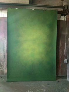 an empty room with a large green painting on the wall and two white bags hanging from the ceiling