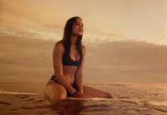 a woman sitting on top of a surfboard in the middle of the ocean at sunset