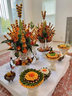 an arrangement of flowers and fruit on a table in a room with windows, rugs and curtains