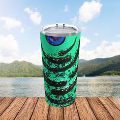 a green cup sitting on top of a wooden table next to a body of water