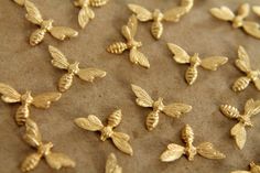 many gold bees are laying on a piece of brown paper and some have been cut into smaller pieces