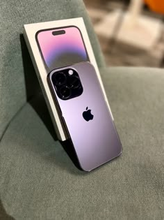 an apple phone sitting on top of a green chair next to a cardboard box with the cover open