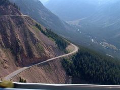 a view from the top of a mountain looking down at a winding road with trees on both sides