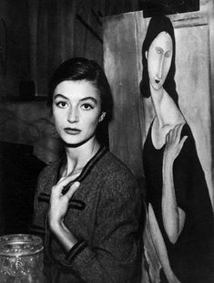 a black and white photo of a woman in front of a painting with her hand on her chin