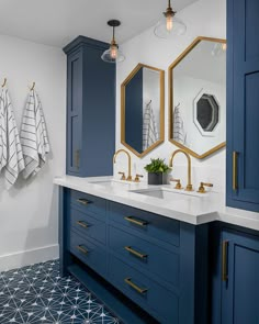 a bathroom with blue cabinets and white counter tops, two mirrors on the wall and gold accents