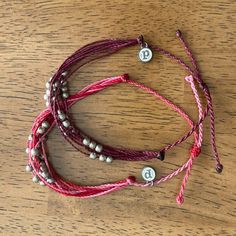 three bracelets with silver beads and pink cords on a wooden surface, one has a button