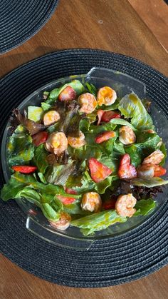 a salad with shrimp and lettuce in a glass bowl on a wooden table