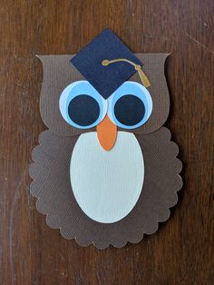 an owl wearing a graduation cap and glasses on top of a wooden table with paper cut outs