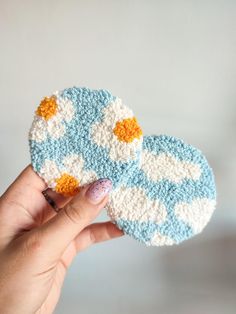 two crocheted coasters in the shape of clouds are being held by a woman's hand