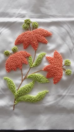 an embroidered piece of art with flowers and leaves on a white cloth background, in the shape of a flower