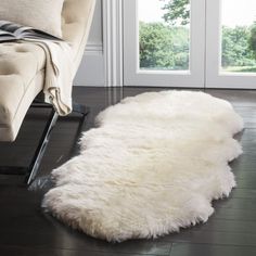 a white sheepskin rug is on the floor in front of a chair and window